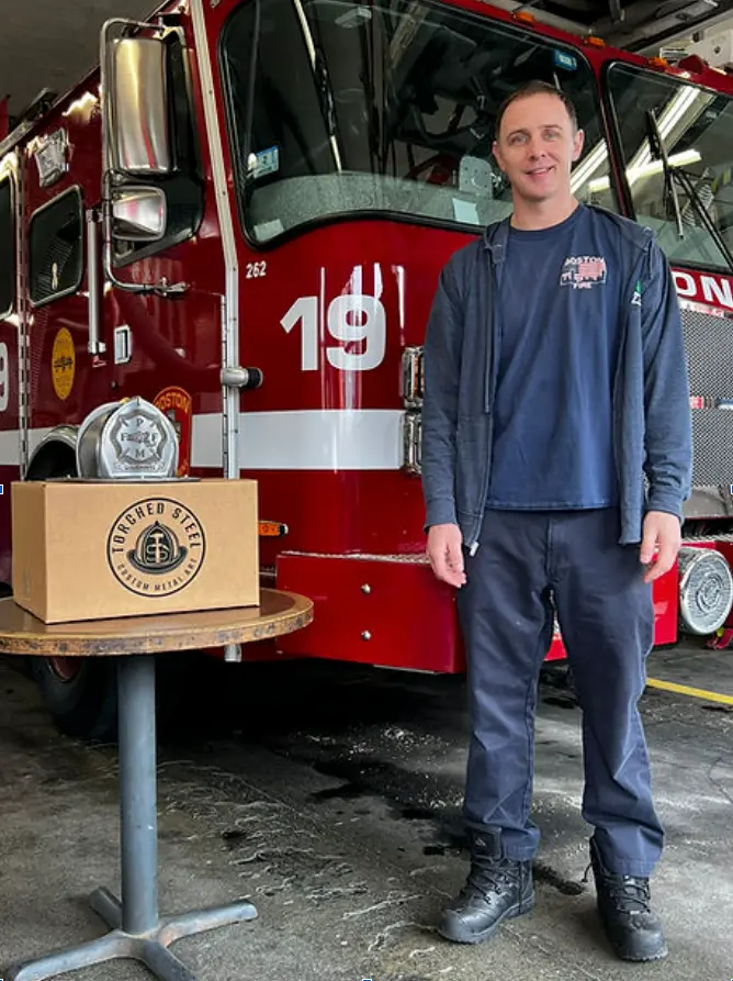 Dan, founder of Torched Steel, with a branded box in front of a fire engine at his firehouse